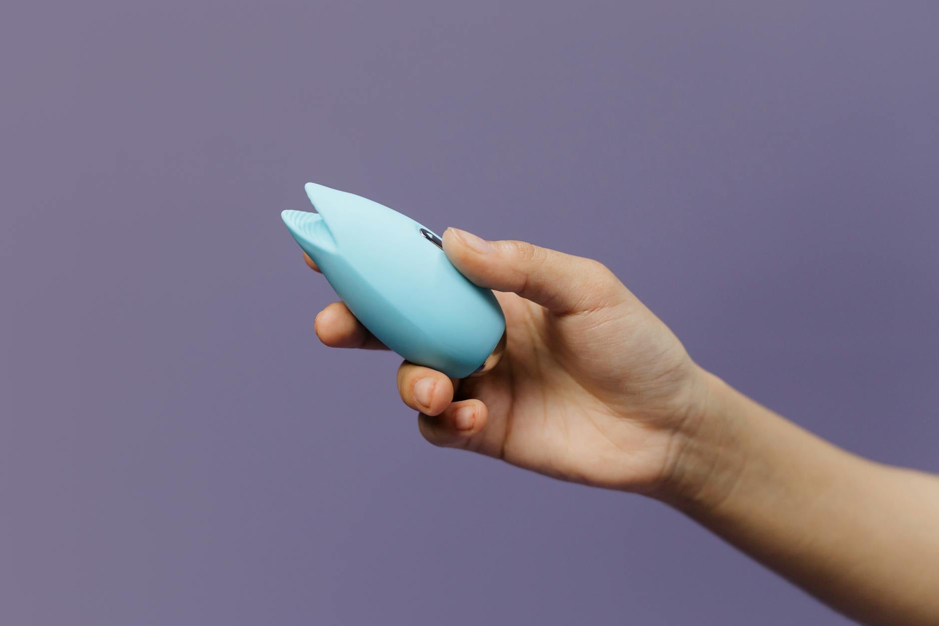 Vibrador de silicona azul sostenido en la mano contra fondo púrpura sólido, promoviendo el auto-amor y la sexualidad