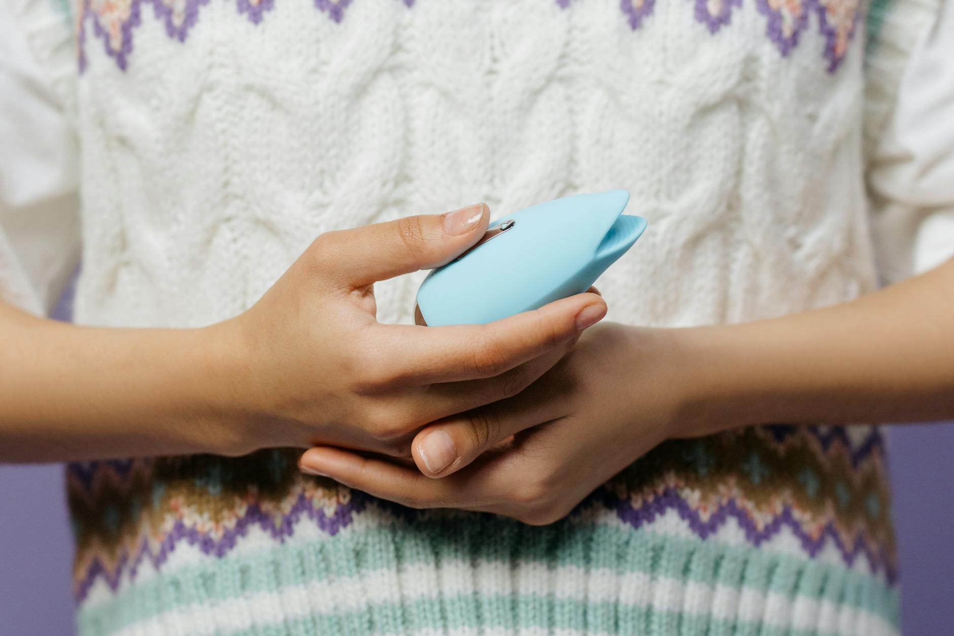 Mano sosteniendo un vibrador azul contra un suéter tejido