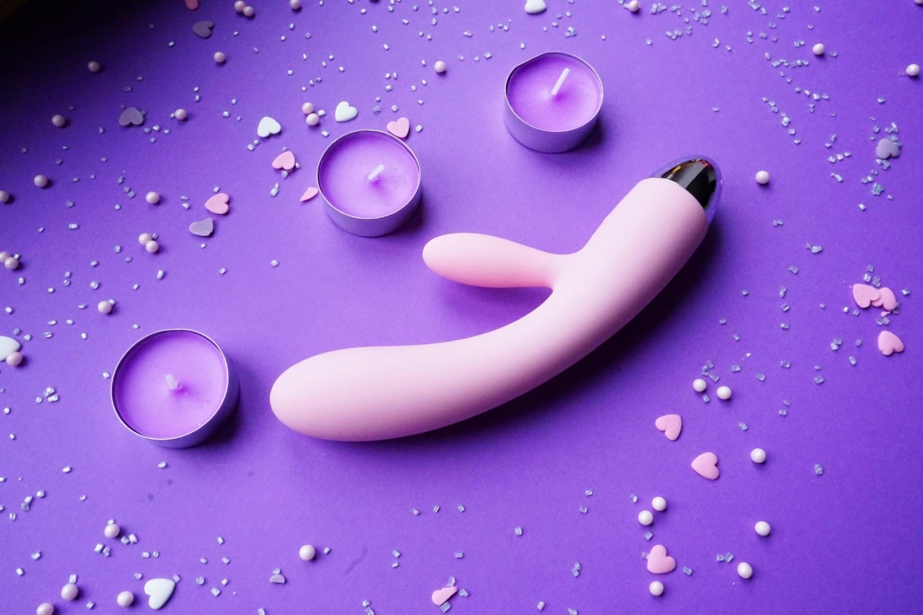 Vibrador rosa sobre fondo púrpura con confeti de corazones y velas para una atmósfera romántica